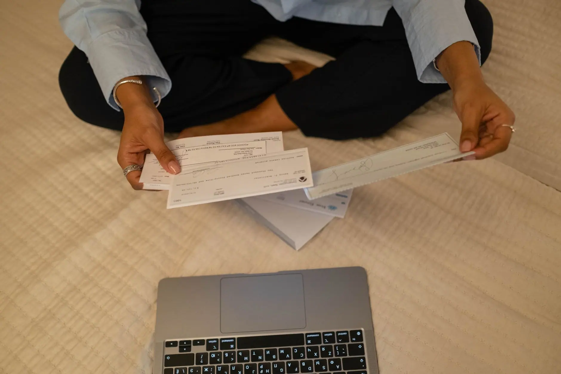 Chèques tenus à la main, posés à côté d'un ordinateur portable